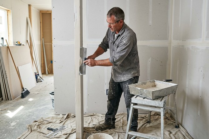 Drywall contractor taping a seam with a wide knife in a freshly hung room